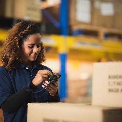 Warehouse worker using bar code scanner on boxed goods inside warehouse.
