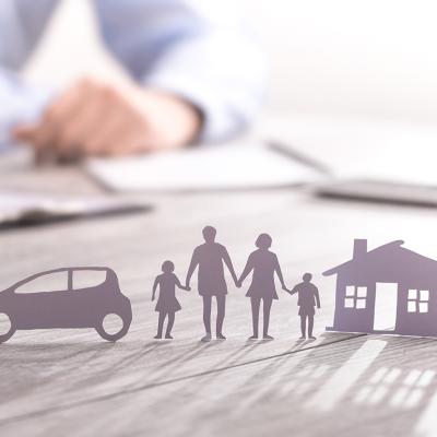 an insurance agent writing in documents with a paper figure of a family with a house and car.