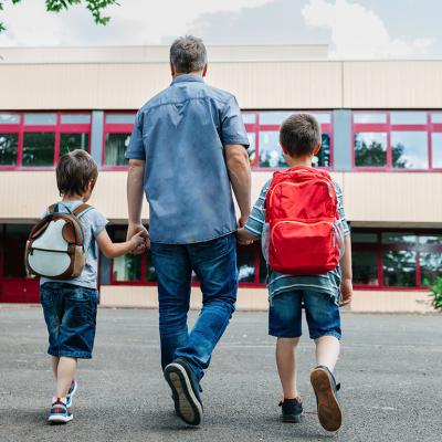 A father holding his two young boys and dropping them back to school.