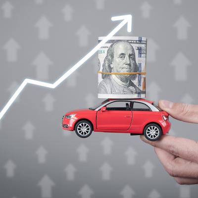 A miniature car with a dollar on top held up with an upward arrow as a concept of rising prices.