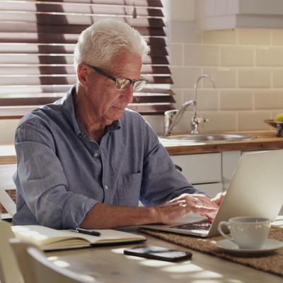 A senior man using a laptop in his kitchen.
