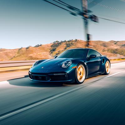 A black Porsche Turbo S driving on a highway with mountains in the background.