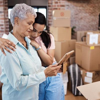 An older woman looking at a photograph while getting a hug from a younger family member while packing boxes on moving day.
