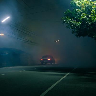 A classic car drives down a spooky road at night.