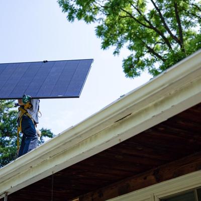 Michael Reimann, installer with Lumina Solar, carries a large panel and his face is not visible while installs solar panels on the roof of a home in Kensington, MD on July 3, 2025.
