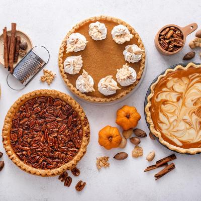 Top-down view of variety of Thanksgiving pies including pumpkin, pecan and cheesecake pumpkin pie on light background.