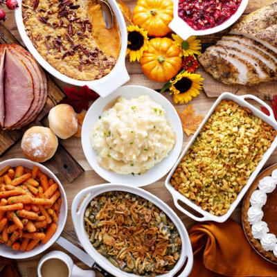 A table full of traditional holiday and Thanksgiving dishes such as mashed potato, ham, turkey, stuffing, and pumpkin pie.