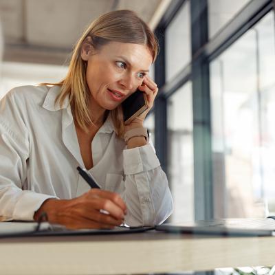 A businesswoman writing down notes as she talks to someone on the phone.