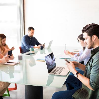 A business team in a meeting room but each member is using their phone.