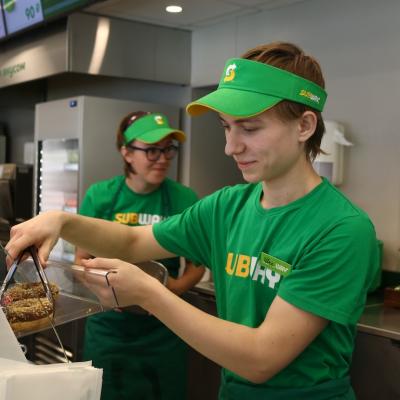 Subway worker grabbing a donut from display container.