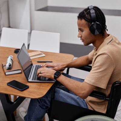 A man in a wheelchair using headphones at a laptop.