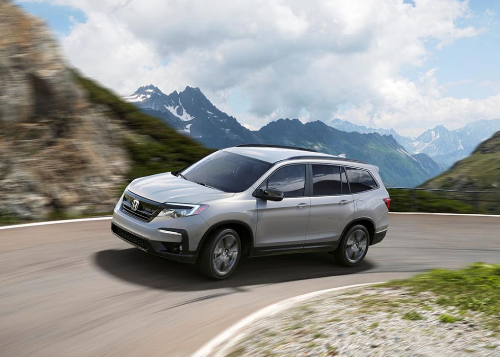 2022 Silver Honda Pilot driving around a curve on a mountain road.