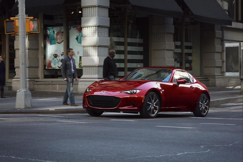 Soul Red Crystal Metallic Mazda Miata MX-5 stopped at an intersection next to a crosswalk.
