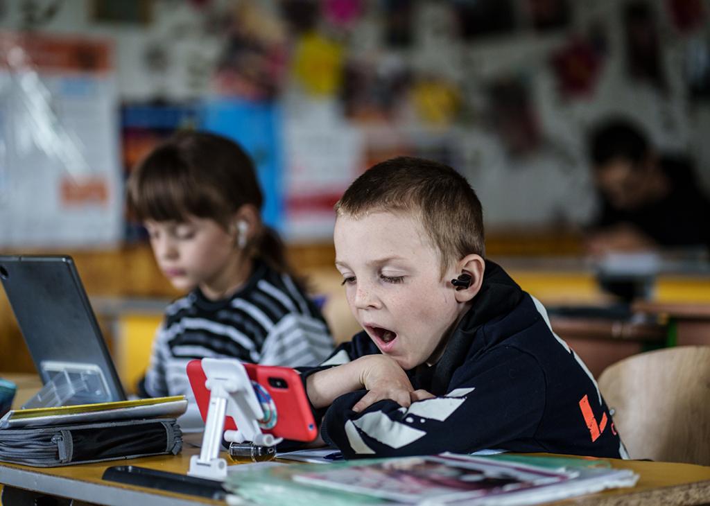 Two young children in a community center using tablets and smartphones for an online class.
