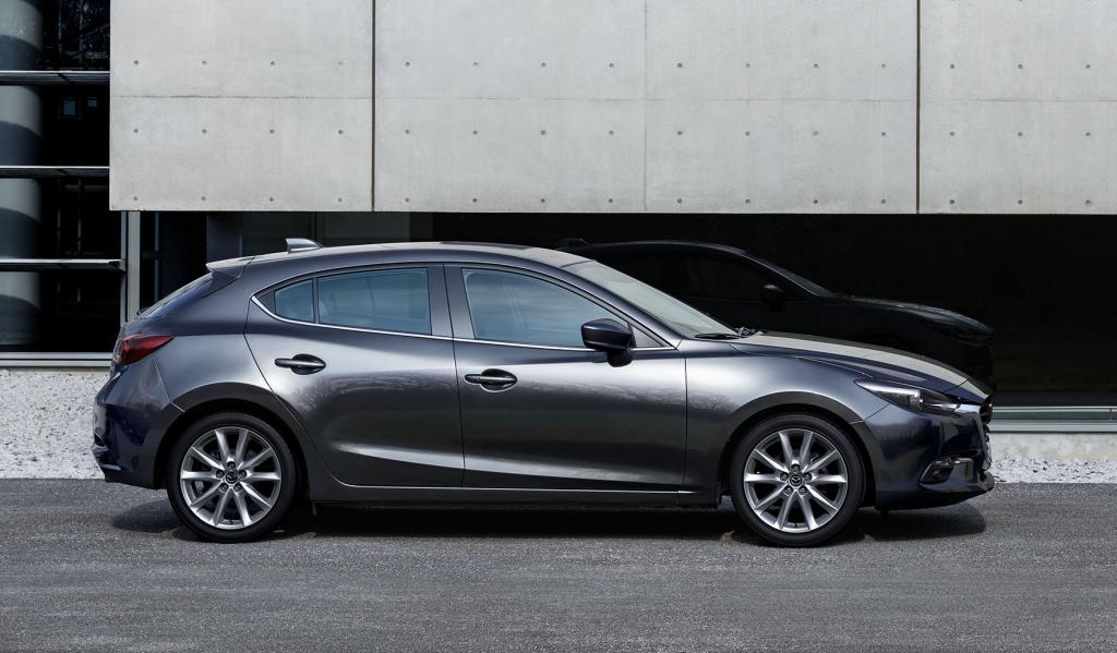 Black Mazda 3 parked in front of concrete building.