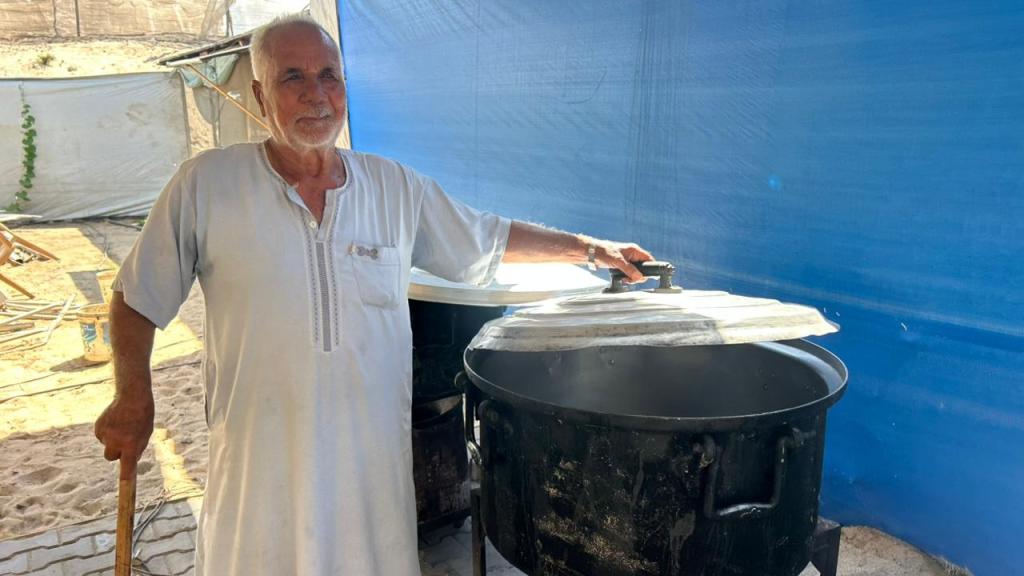 Omran Khamees Al-Astal next to a large pot for cooking with a blue tent background behind him.