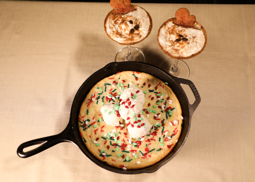 A 'Winter Wonderland' Sugar Cookie on a skillet with two glasses of Gingerbread Espresso Martini.
