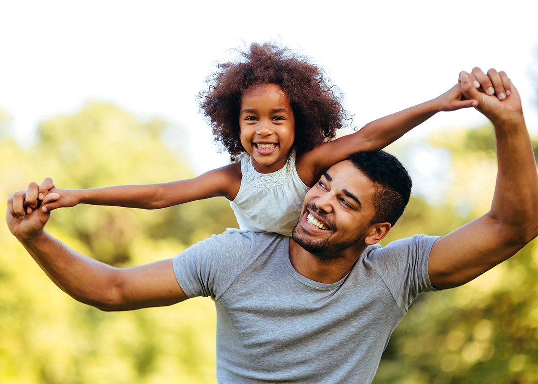 Father carrying daughter on shoulders in park.