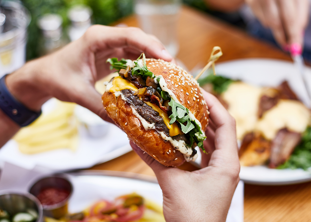 Close up hands holding burger at outdoor restaurant table.