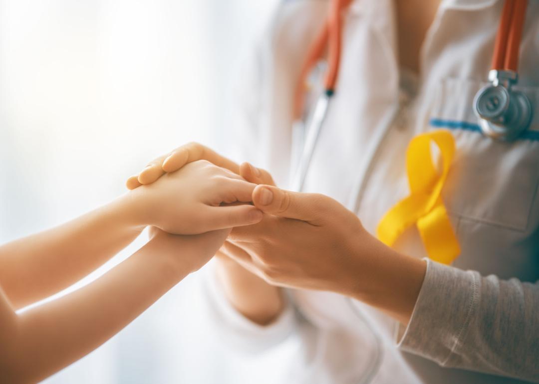 Doctor with yellow childhood cancer awareness ribbon holding child’s hands.
