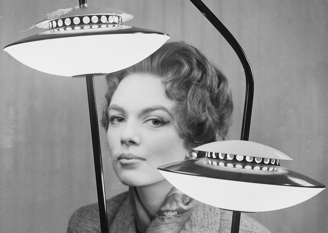 Woman poses behind flying saucer lamp.