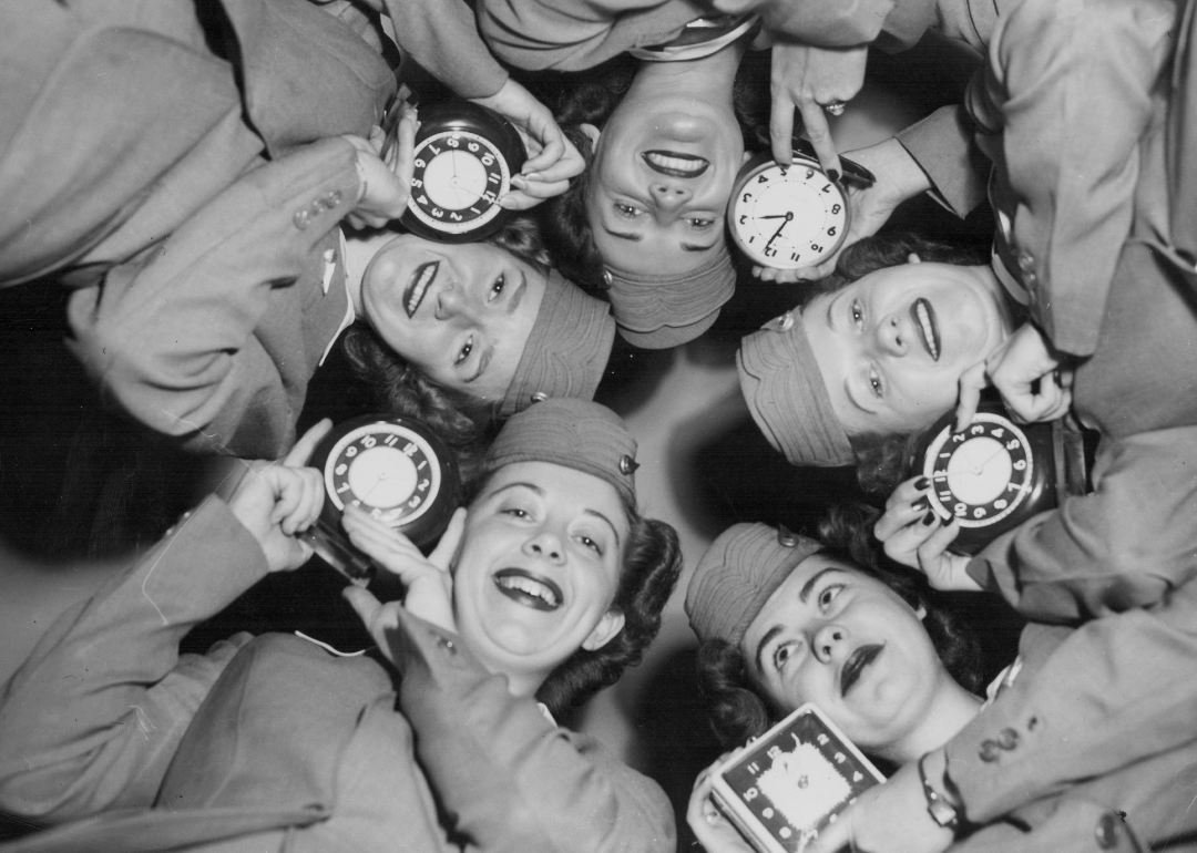 Air line stewardesses posing with clocks before time change.