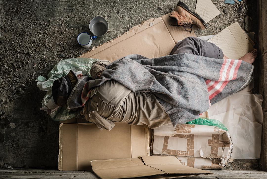 Man wearing sweater and blanket, sleeping on cardboard