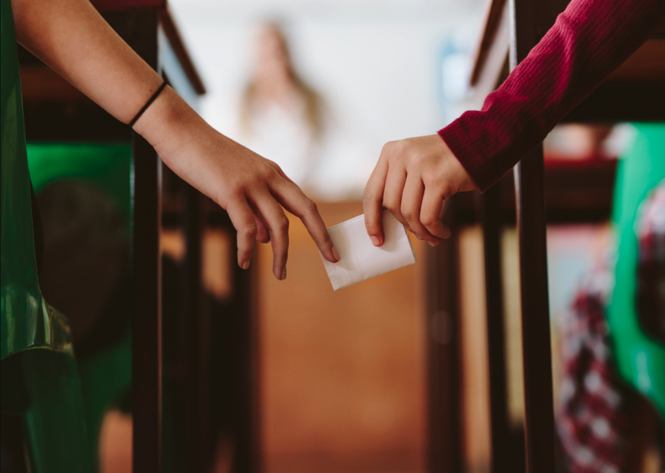 Hands of two students passing a note in class