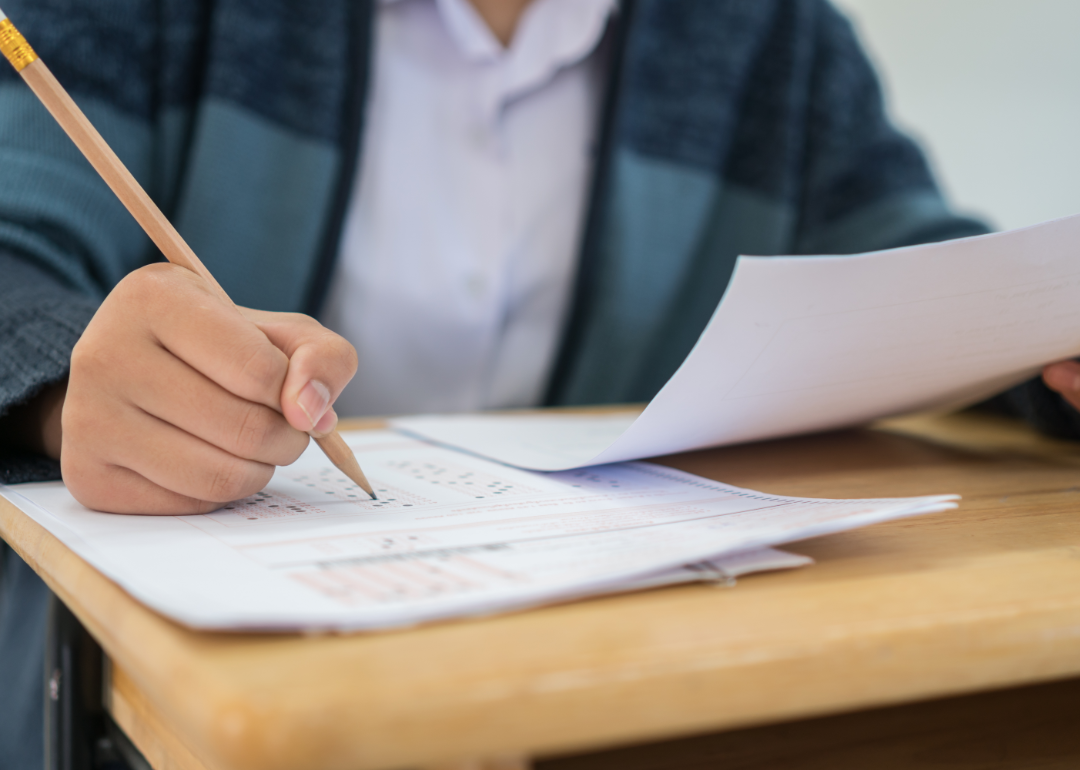 Closeup of student taking an exam at a desk, filling in an answer sheet with a pencil.