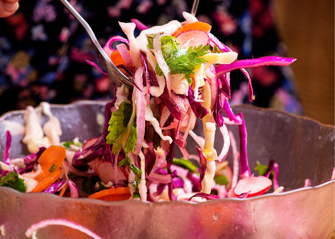 Closeup of someone using fork to pick up slaw from copper serving dish.