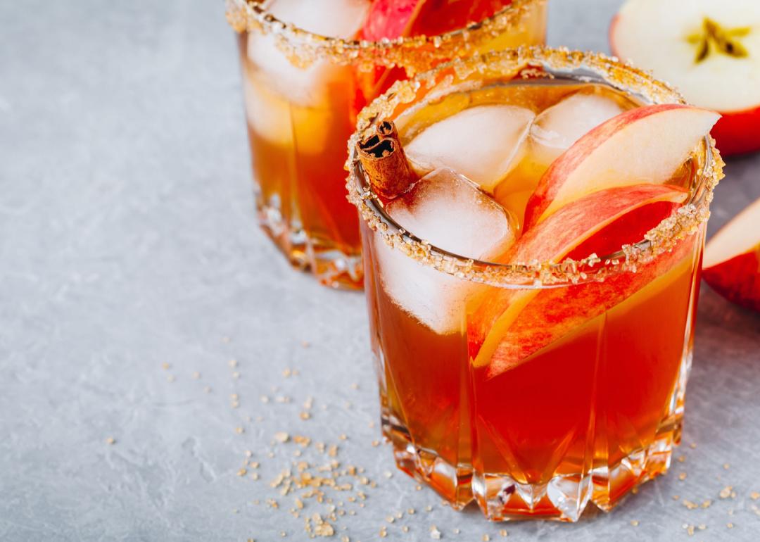 Closeup of apple cider cocktail with salt on the rim, apple slices, and ice.