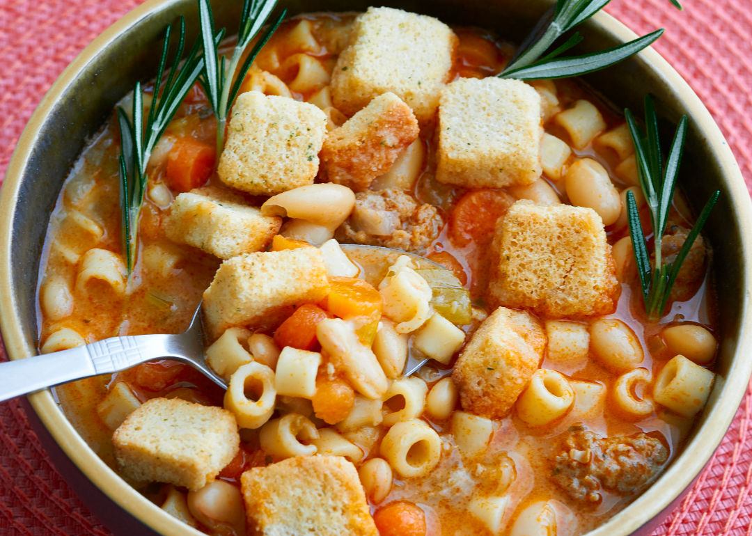 Closeup of bowl of pasta e fagioli soup with sprigs of rosemary in a bowl on a pink placemat.