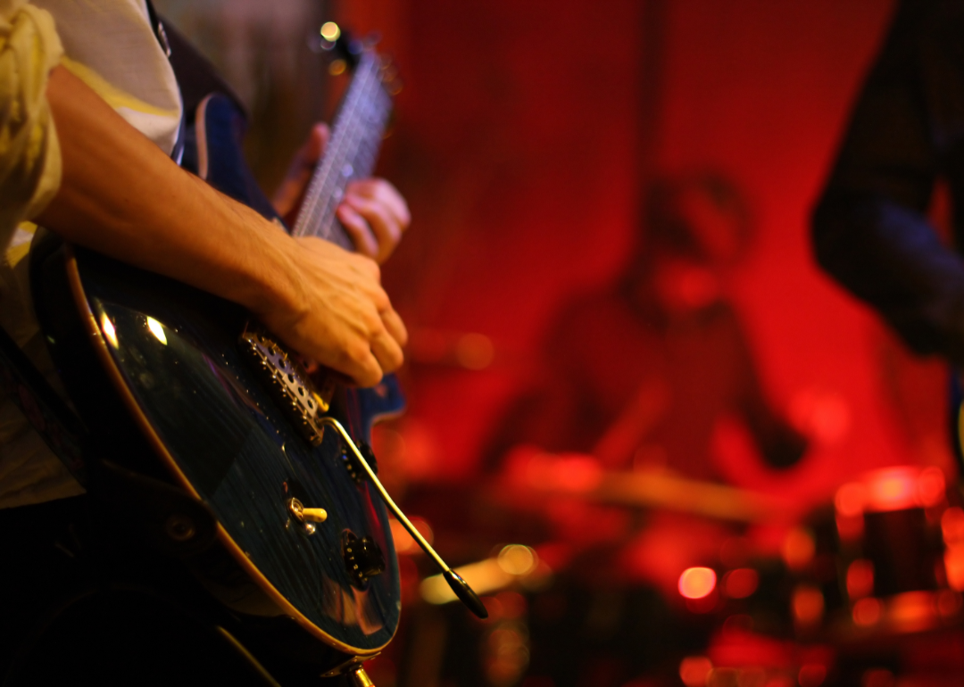 Person playing guitar at the forefront of a band in a bar.