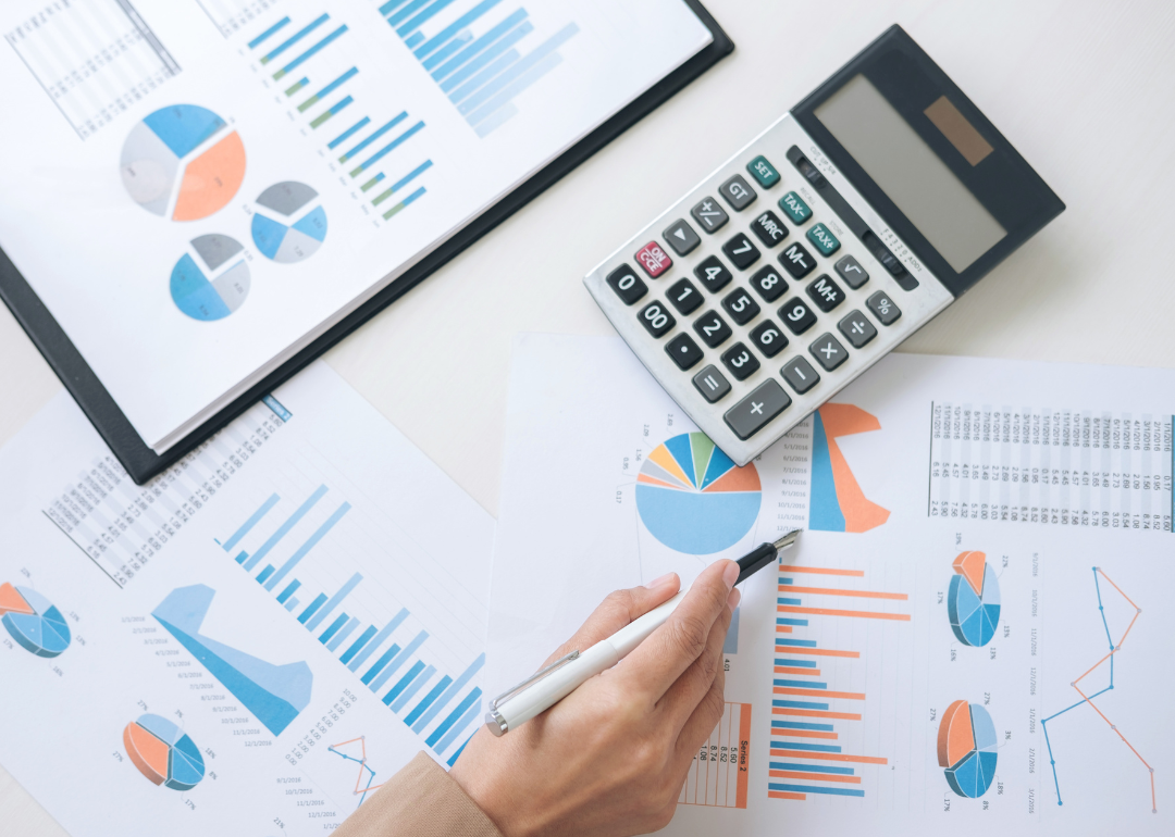 A women works at a desk covered with financial charts and calculator.