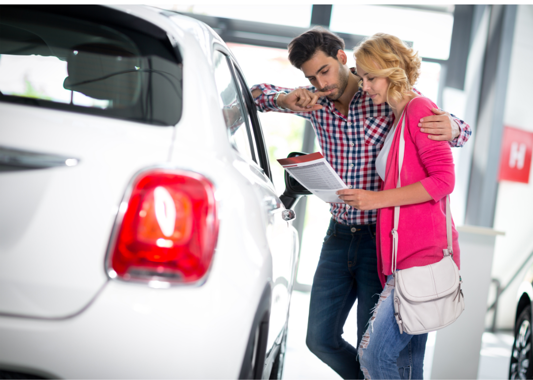 A couple look over paperwork in a car dealership as they shop for a vehicle.