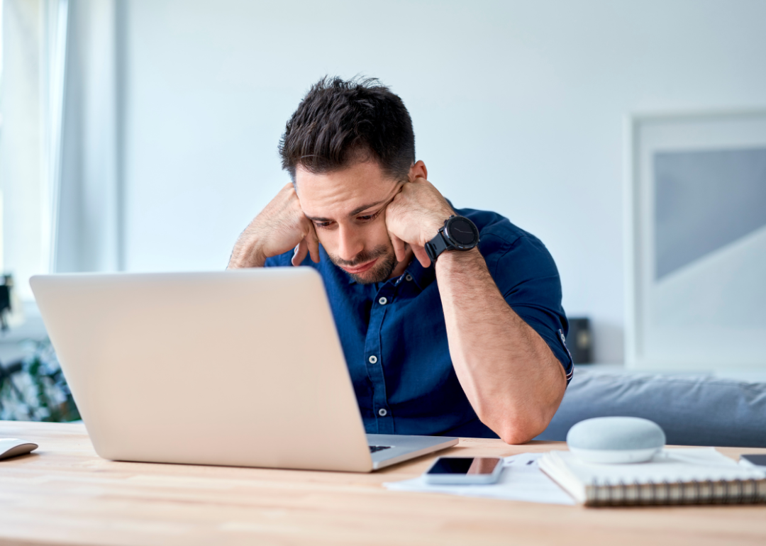 A young man sits at a desk and stares, discouraged, at a laptop