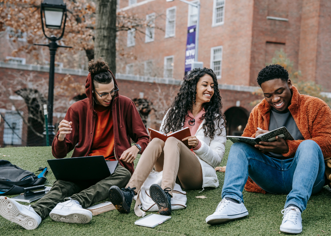 A group of three multiethnic students sit together on a college quad