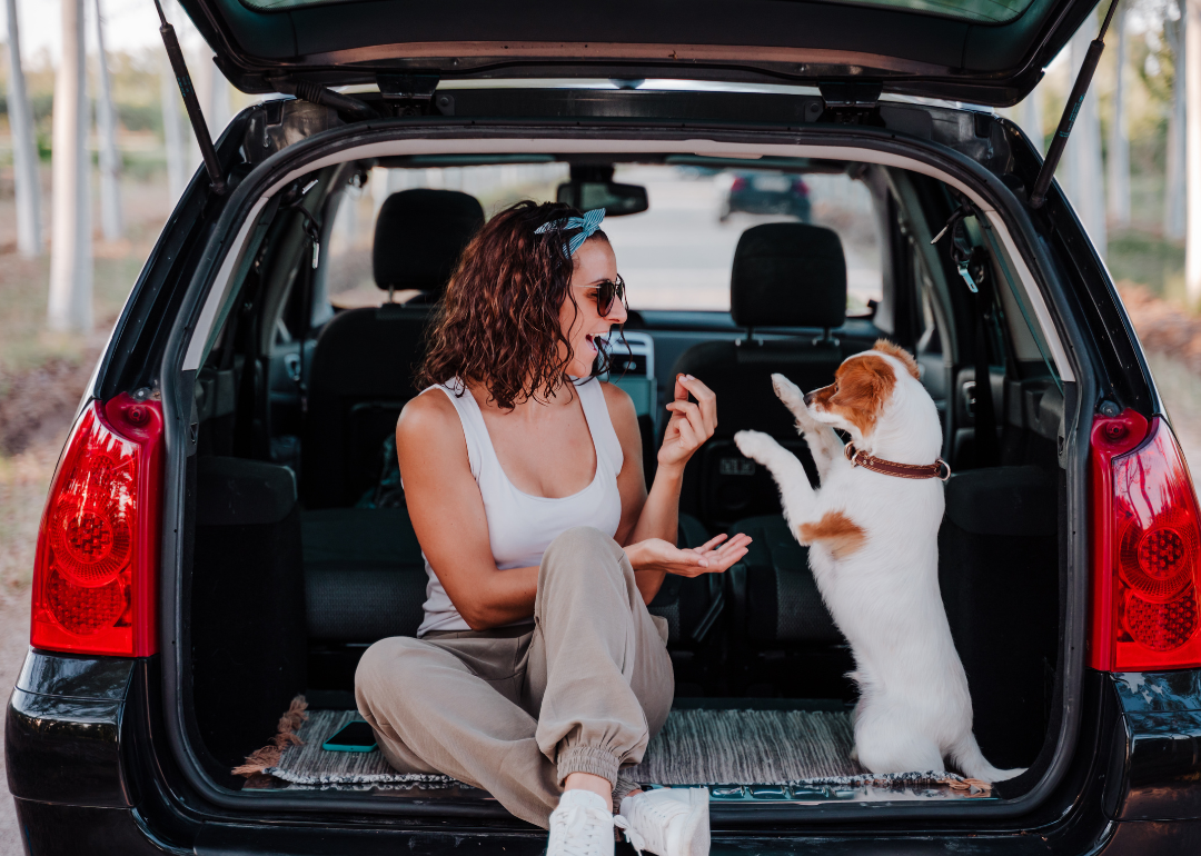 A woman and dog sit in the open rear cab of an SUV, playing.