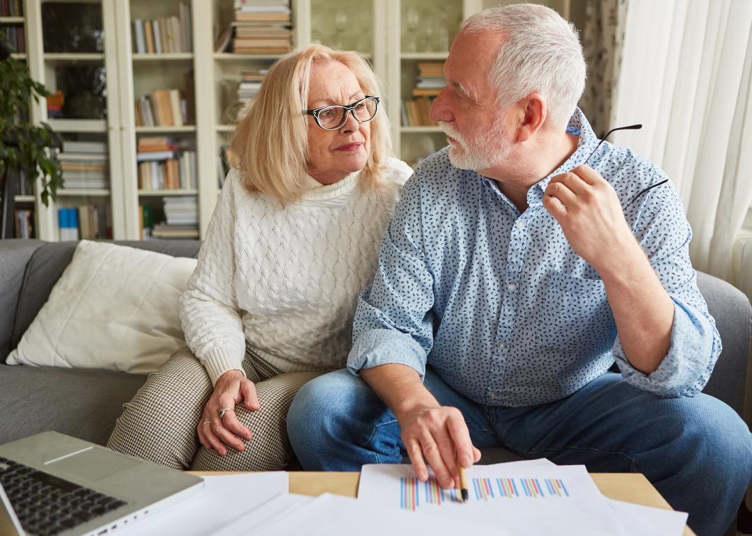 An older couple sit together on a couch going over financial paperwork.