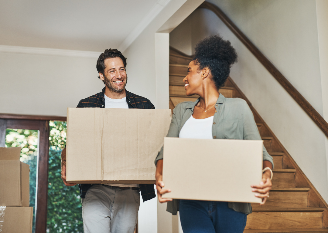 A young couple is carrying cardboard boxes into their new home.