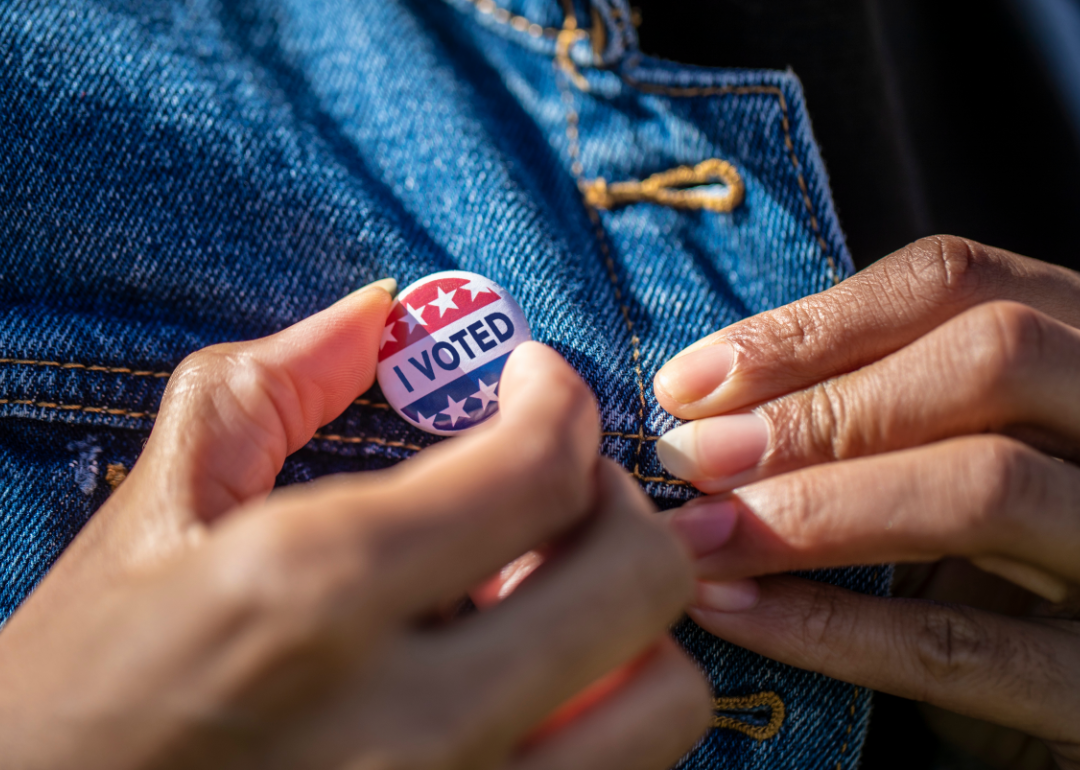 Hands attaching an "I Voted" pin to a denim jacket.
