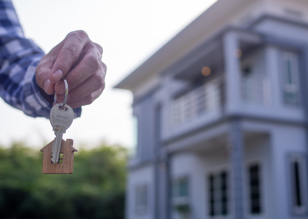 Hand holding a new house key with a blue and white house in the background.