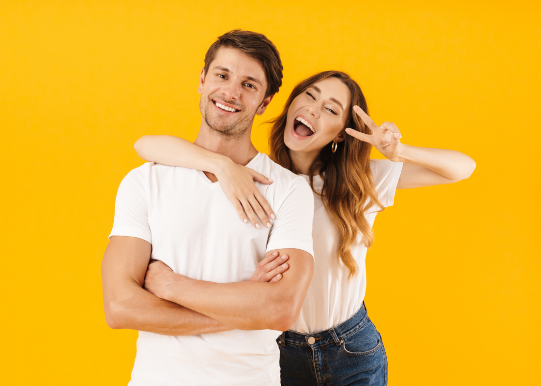 A young couple smiling; the woman holds up a peace sign