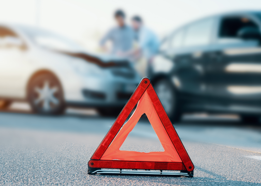 A red triangular hazard sign sits on the road near an auto crash