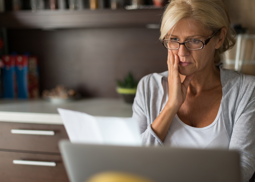A woman sits at a desk and looks worriedly at a bill she's received
