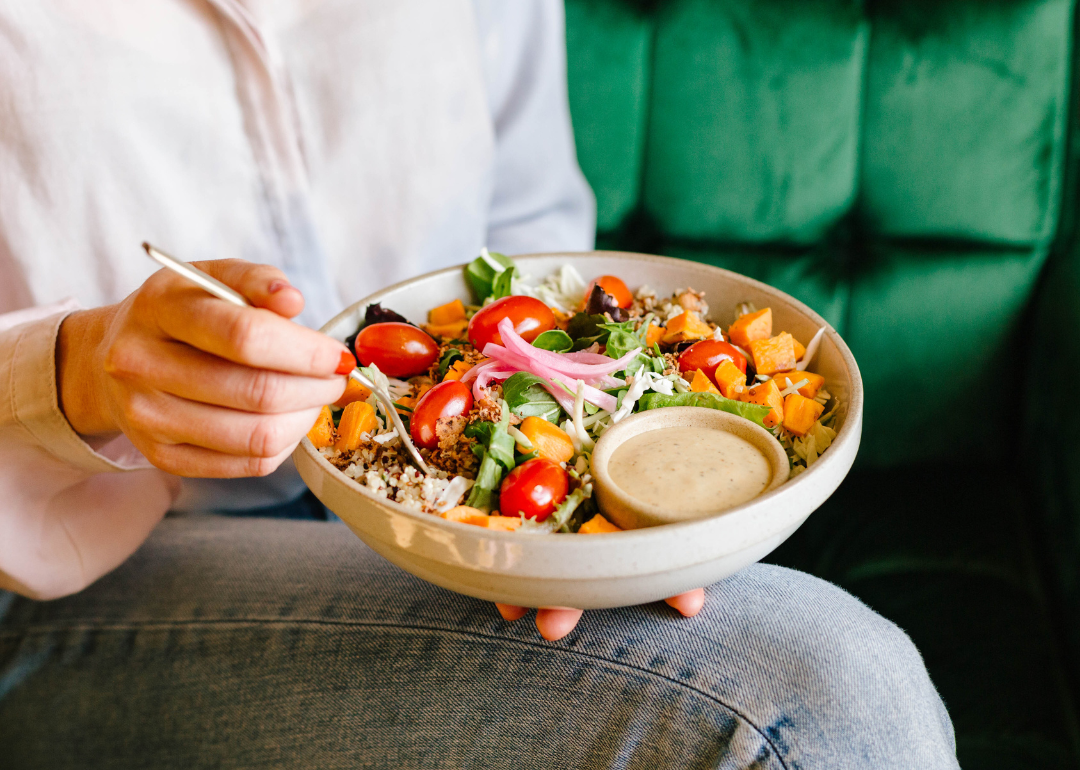 A person eats a bowl of assorted vegetables .
