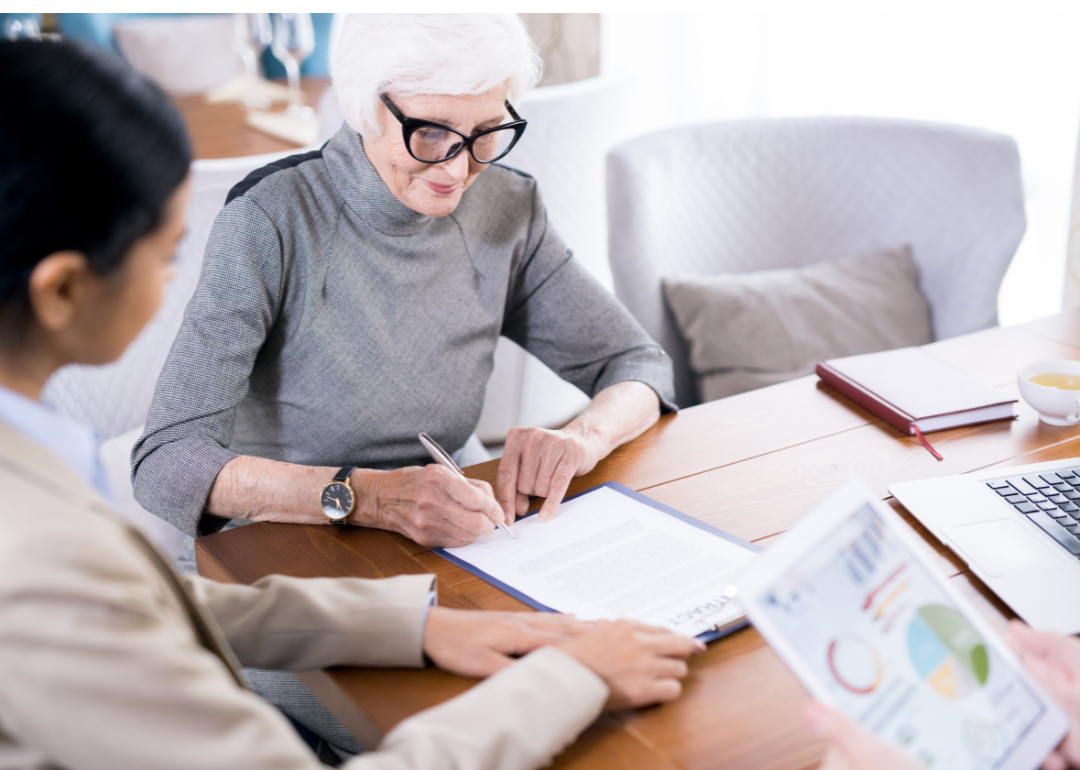 A older woman in a gray sweater fills out a will