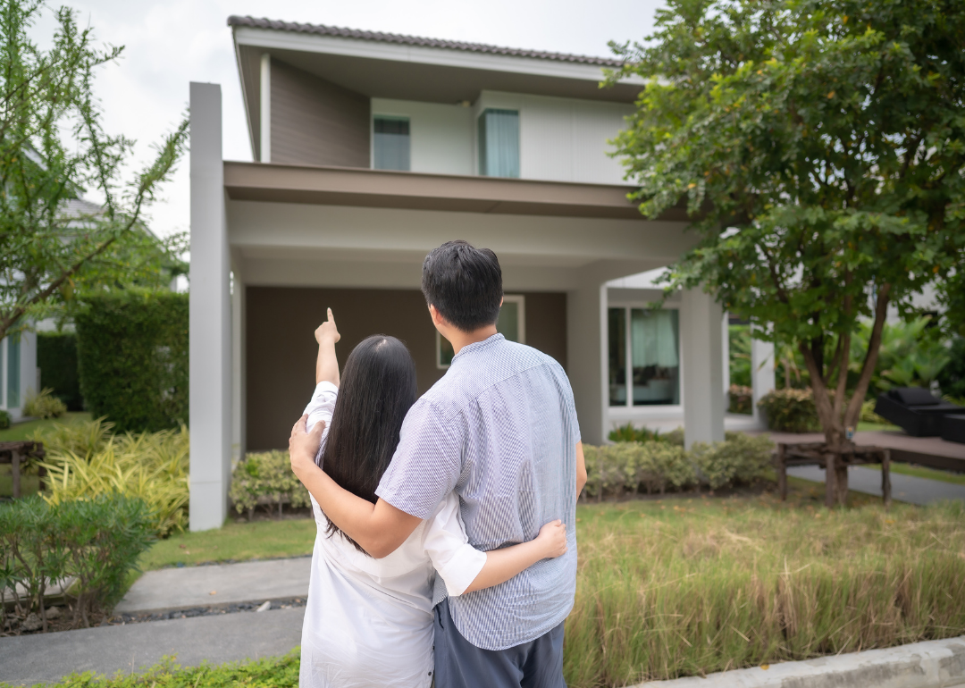 A couple in front of a house, the woman pointing up toward it