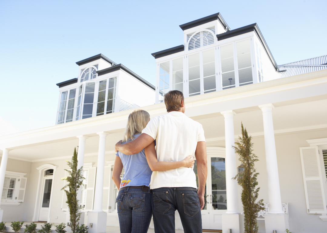 A young couple stands in front of a white two-story house