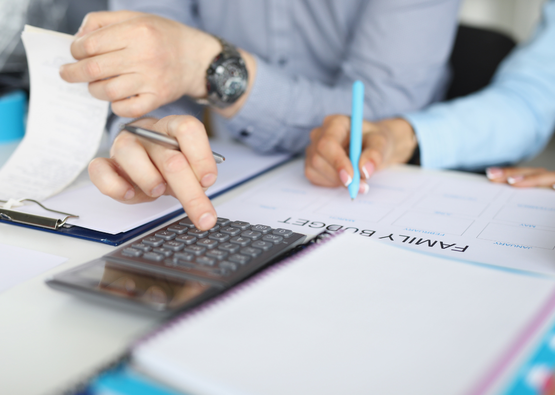 The hands of two people who are using a calculator and pen to make a family budget
